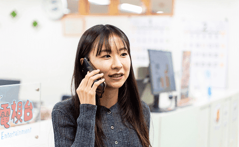 スマートフォンで連絡を取りながら笑顔で業務に取り組む女性スタッフ。モダンで明るいオフィス環境で、コミュニケーションを大切にする職場の雰囲気